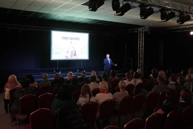 Vīrietis zālē pasniedz auditorijai lekciju